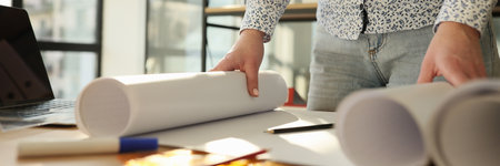 Woman architect standing near work desk with rolls of blueprintsの写真素材