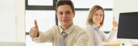 Man and woman showing thumbs up signs in officeの写真素材