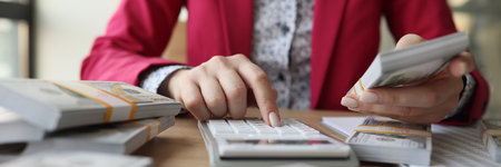 Woman counting money on calculator and holding wad of moneyの写真素材