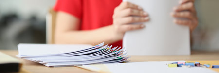 Woman holds stack of white paper sheets sitting at tableの写真素材