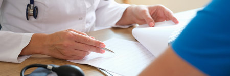 Doctor writes treatment plan for patient sitting at tableの写真素材