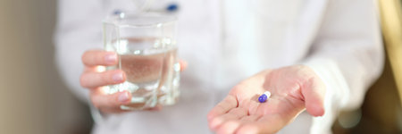 Doctor in uniform holds pill and glass of water in handsの写真素材