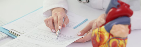 Cardiologist reads patient test results at table in hospitalの写真素材