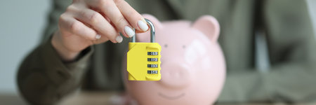 Woman holds combination padlock in front of piggy bankの写真素材