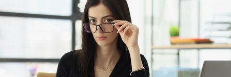Woman with glasses sits at desk in officeの写真素材