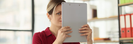 Woman employee lifts clipboard holding in hands hiding faceの写真素材