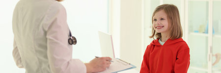 Doctor with clipboard examines little girl in officeの写真素材