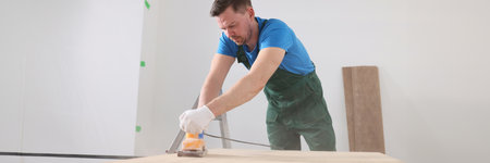Focused carpenter polishes wooden board surface in roomの写真素材