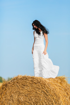 Young woman standing on a hay bale against a blue skyの写真素材