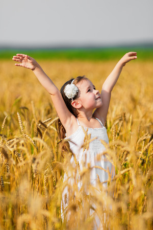 Little girl throwing her arms up among wheat earsの写真素材