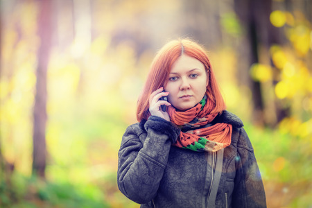 Portrait of beautiful smiling red-haired woman talking by mobile phone (shallow dof)の写真素材