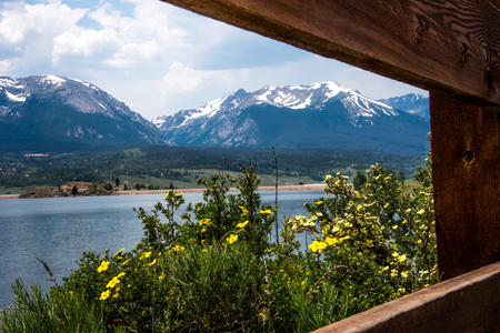 A wooden fence forms a frame for a beautiful view of flowers, lake and mountainsの写真素材