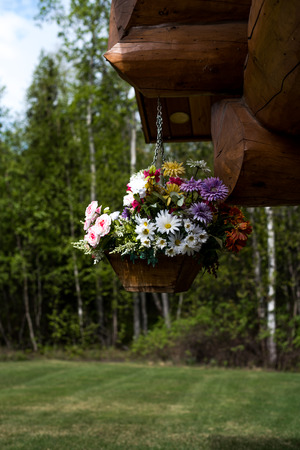 Flower basket full of flowers hanging from front porch of log cabinの写真素材