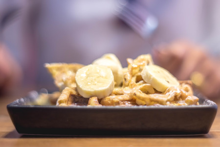 Toast topped with sliced bananas, nuts, egg, cream cheese sauce. Extreme shallow depth of field with selective focus on toast and some blur on corner of plate. Woman / man using a fork to eat.の写真素材