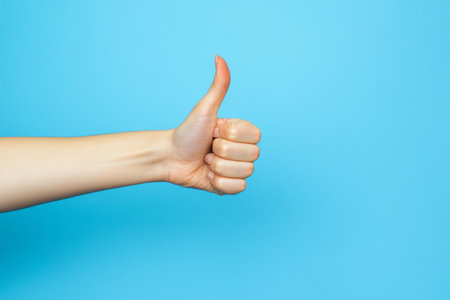 Close-up of a hand showing a thumbs-up gesture against a bright blue background. A simple and positive visual conveying approval or success.の素材