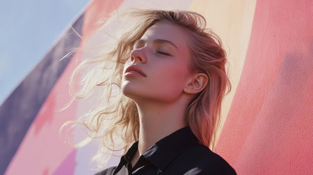 A tranquil blond woman leans against a soft pink wall, eyes closed, embodying serenity and introspection in a soothing, pastel-hued atmosphere.の素材