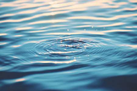 A close-up view of a water droplet resting on the surface of a larger body of water, reflecting light and creating a mesmerizing visual effect.の素材