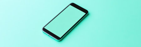 Black cell phone with a green screen resting on a blue surface,.の素材