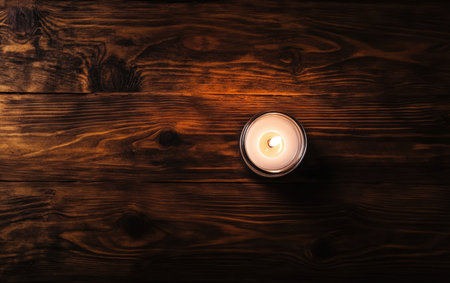 A lit candle rests on a wooden table, casting a warm glow in the surrounding space.,の素材