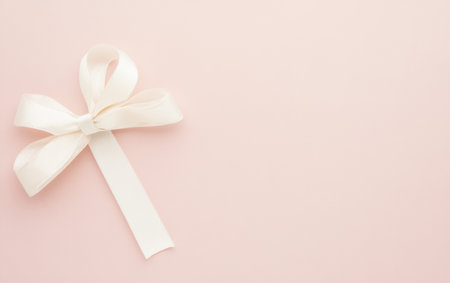 A white ribbon tied in a bow against a soft pink background.,の素材