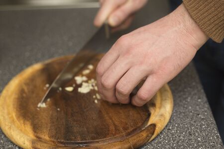 Man cutting garlic with a knife. Vegetable prepring in the kitchen bord. Healhy chopping ingreient.