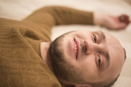 Portrait of a bristles man. The guy resting on the bed. Smile and happy.