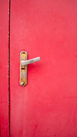 Red closed door with old handle. Rusty hardware with a lock. Worn paint on metal.の写真素材