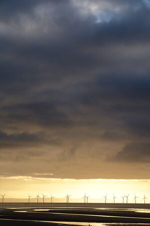 A row of offshore wind turbines beneath a cloudy stormy sky