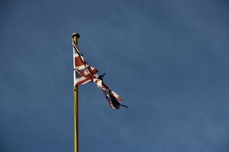 An old, worn and tattered UK Union Flag, or Union Jack flag set against a blue skyの写真素材