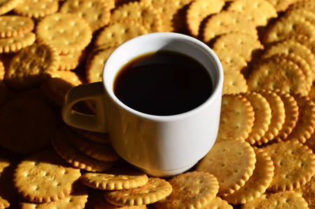 Background image of a small white cup of coffee and classic salty cracker on a brown wooden table with copyspaceの写真素材