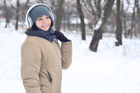 Portrait of pretty attractive caucasian pierced girl hipster winter park. She is listening to music on headphones. Youth street fashion. Winter fun. Walks in the open airの写真素材