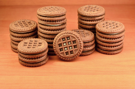 Heap of chocolate chip cookies filled with vanilla white cream lies on wooden brown surface. Sweet and tasty sandwich round biscuits. Detailed food photography with copyspaceの写真素材