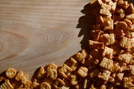 A small pile of salty crackers in the form of printed English letters, which lie on a wooden...