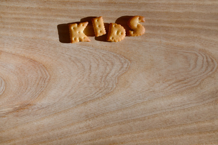Kids. Text from the salty crackers as printed English letters that lie on a wooden chopping board. Message, lined with edible lettersの写真素材