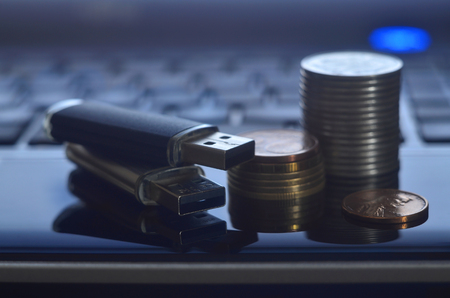 USB memory cards and a few coins lying on the body of black laptop in front of his keyboard. Virtual memory storage with USB output and a small amount of moneyの写真素材