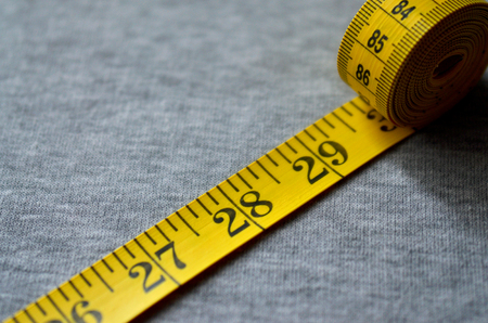 Yellow measuring tape with numerical indicators in the form of centimeters or inches lies on a gray...