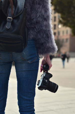 Rear view of a female photographer with a modern SLR camera in her hand against a blurred crowded streetの写真素材