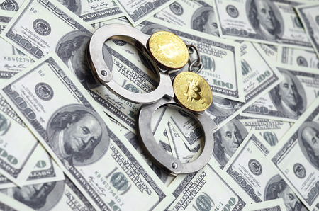 Police handcuffs and bitcoins lie on a large number of dollar bills. The concept of problems with the law during the illegal cryptocurrency mining and bitcoin operationsの写真素材