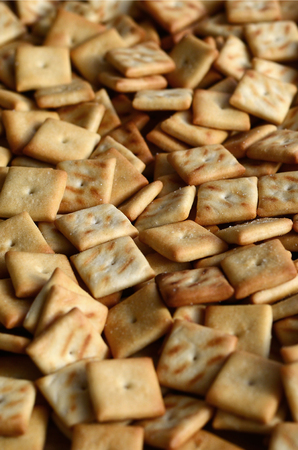 A lot of small cookies are square shaped. A pattern of a yellow salt cracker. Background image with salted pastryの写真素材