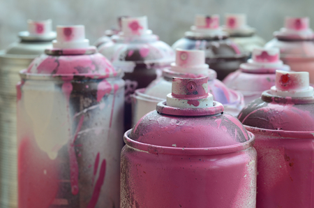 A lot of dirty and used aerosol cans of bright pink paint. Macro photograph with shallow depth of field. Selective focus on the spray nozzleの写真素材