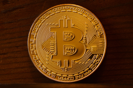 One new golden physical bitcoin is lies on dark wooden backgound, close up. High resolution photo. Cryptocurrency mining conceptの写真素材
