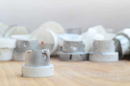 Several plastic nozzles from a paint sprayer that lie on a wooden surface against a gray wall background. The caps are smeared in chrome paint. The concept of street art and graffitiの写真素材