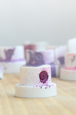 Several plastic nozzles from a paint sprayer that lie on a wooden surface against a gray wall background. The caps are smeared in violet paint. The concept of street art and graffitiの写真素材