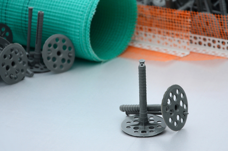 A set of construction items for the insulation of walls. Plastic dowels, a roll of mesh for the insulation of facades and a corner profile with a grid lie on the foam polystyrene surfaceの写真素材