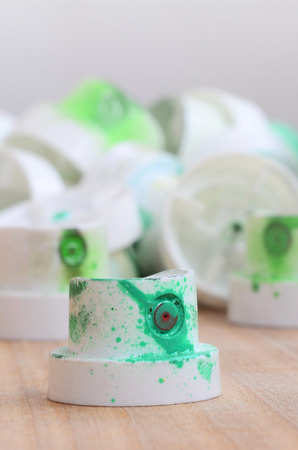 Several plastic nozzles from a paint sprayer that lie on a wooden surface against a gray wall background. The caps are smeared in green paint. The concept of street art and graffitiの写真素材