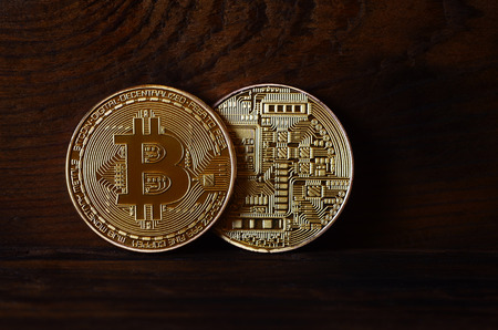 Two new golden physical bitcoins lies on dark wooden backgound, close up. High resolution photo. Cryptocurrency mining conceptの写真素材