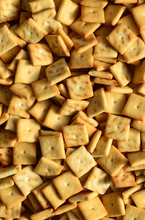 A lot of small cookies are square shaped. A pattern of a yellow salt cracker. Background image with salted pastryの写真素材