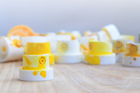 Several plastic nozzles from a paint sprayer that lie on a wooden surface against a gray wall background. The caps are smeared in yellow paint. The concept of street art and graffitiの写真素材