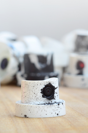 Several plastic nozzles from a paint sprayer that lie on a wooden surface against a gray wall background. The caps are smeared in black paint. The concept of street art and graffitiの写真素材