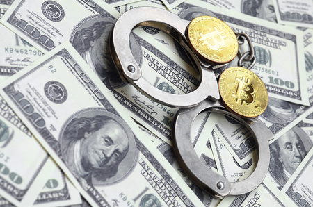 Police handcuffs and bitcoins lie on a large number of dollar bills. The concept of problems with the law during the illegal cryptocurrency mining and bitcoin operationsの写真素材